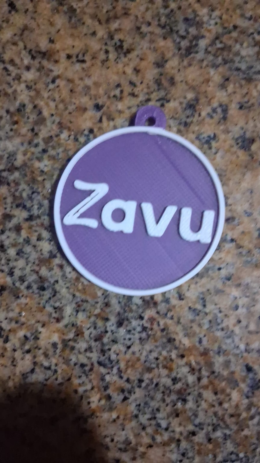 Peça circular da ZAVU, roxa, com nome branco em relevo.